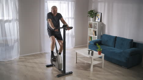 modern-stationary-bicycle-for-training-at-home-middle-aged-man-is-using-it-for-keeping-fit-and-health-cardio-workouts